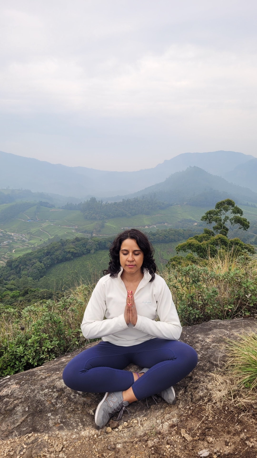 Janisha Parmar meditating on a mountain overlooking misty hills